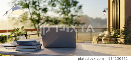 Laptop on wooden table with lamp and book aside at sunlight terrace or balcony of cafe or restaurant Laptop on wooden table with lamp and book aside at sunlight terrace or balcony of cafe or restaurant 134130331