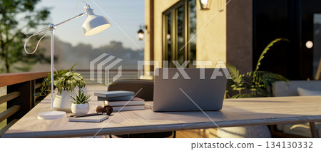 Laptop on wooden counter with lamp and book aside at the sunlight terrace of cafe or restaurant 134130332