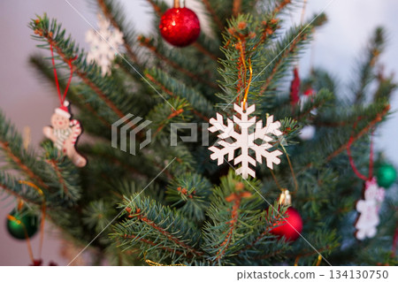 a Christmas tree decorated with a white snowflake ornament, red baubles, and festive hanging figures 134130750