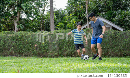 Father and son having fun playing soccer or football in their home's backyard or green grass field. 134130885