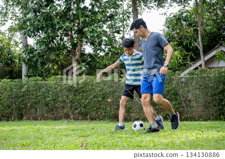 Father and son having fun playing football together in their home's backyard or green grass field. 134130886