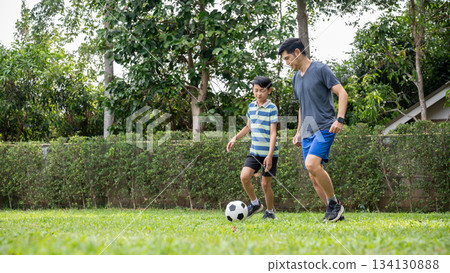 Father and a son playing football or soccer together in their home's backyard or a green grass field. 134130888