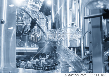 The  empty drinking water bottles  hanging on the overhead conveyor belt for filling process in the light blue scene. 134131885