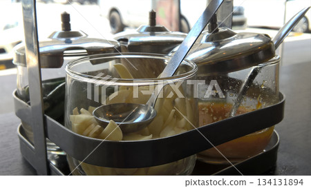 Pickled garlic chili sugar vinegar condiment glass metal spoon jar tray street cafe counter savory sour sweet spicy liquid 134131894