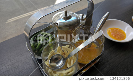 Condiment caddy glass jar metal holder toothpick chili garlic green bean sauce spoon on table near window, cozy mood Condiment caddy glass jar metal holder toothpick chili garlic green bean sauce spoon on table near window, cozy mood 134131896