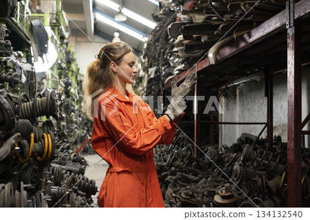 Female technician worker working in garage scrap yard old car part workshop warehouse. 134132540