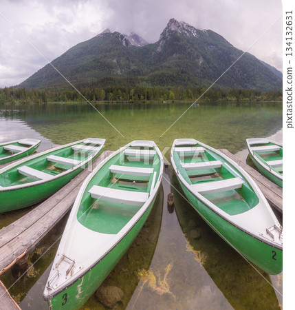 Green rowboats moored to wooden docks on clear mountain lake with forest and peaks in background Green rowboats moored to wooden docks on clear mountain lake with forest and peaks in background 134132631