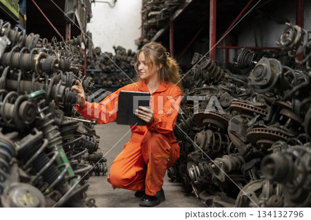 Female technician worker checking inventory with tablet device in garage scrap yard old car part workshop warehouse. 134132796