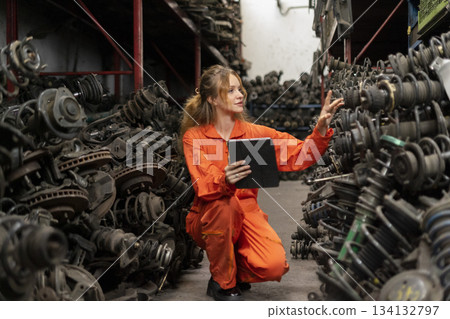 Female technician worker checking inventory with tablet device in garage scrap yard old car part workshop warehouse. 134132797