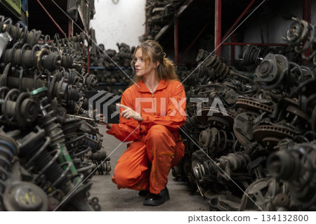 Female technician worker checking inventory with tablet device in garage scrap yard old car part workshop warehouse. Female technician worker checking inventory with tablet device in garage scrap yard old car part workshop warehouse. 134132800