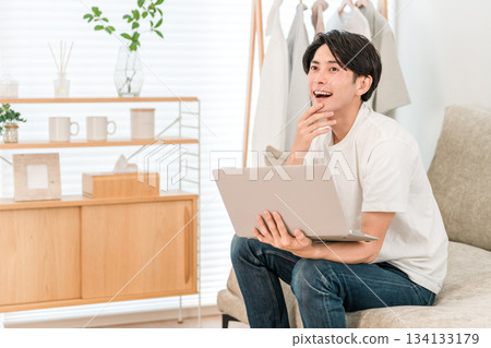 A young Asian man sitting on a sofa and using a laptop (discovery, finding, point, idea) A young Asian man sitting on a sofa and using a laptop (discovery, finding, point, idea) 134133179
