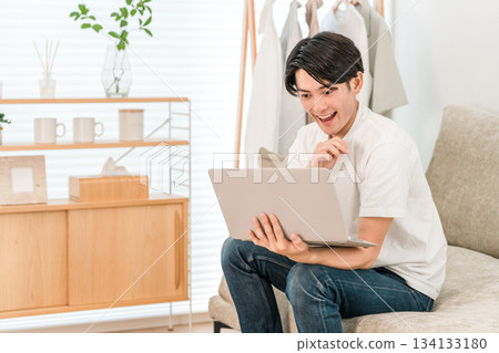 A young Asian man sitting on a sofa and using a laptop (discovery, finding, point, idea) A young Asian man sitting on a sofa and using a laptop (discovery, finding, point, idea) 134133180
