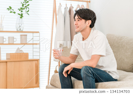 Young Asian man sitting on the sofa in the living room drinking mineral water 134134703