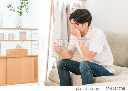 Young Asian man sitting on the sofa in the living room drinking mineral water Young Asian man sitting on the sofa in the living room drinking mineral water 134134706