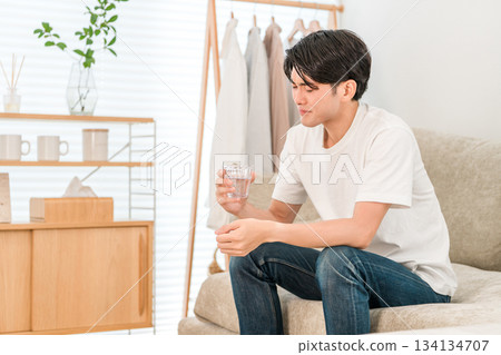 Young Asian man sitting on the sofa in the living room drinking mineral water Young Asian man sitting on the sofa in the living room drinking mineral water 134134707