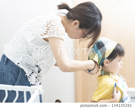 一位母親正在為兒子穿戴背帶和圍裙 一位母親正在為兒子穿戴背帶和圍裙 134135291