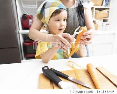 Mother and son peeling carrots together in the kitchen Mother and son peeling carrots together in the kitchen 134135296