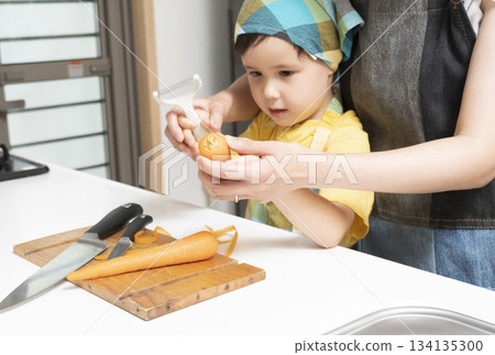 Mother and son peeling carrots together in the kitchen Mother and son peeling carrots together in the kitchen 134135300