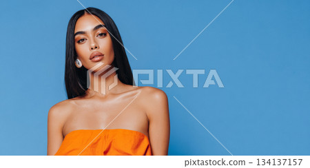 Woman in orange top poses against a blue background showcasing fashion and beauty in studio lighting 134137157
