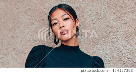 Young woman posing confidently against textured wall in stylish black outfit during daylight 134137398