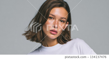 Young woman with short hair poses confidently in a plain white shirt against a gray background 134137476