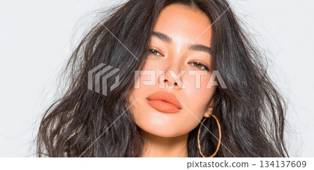 Model poses with long, wavy hair and bold makeup, showcasing confidence in a studio setting with a simple backdrop for a fashion shoot 134137609
