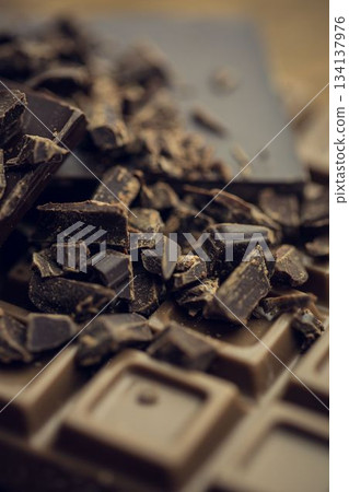 3D render is showing broken dark chocolate bar on wooden tabletop with shards and cocoa dust 134137976