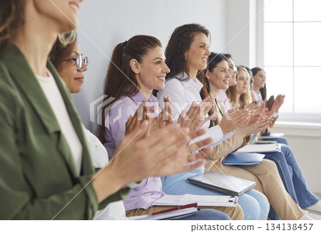 Smiling happy diverse group of business women sitting in a row on meeting and applauding. Smiling happy diverse group of business women sitting in a row on meeting and applauding. 134138457