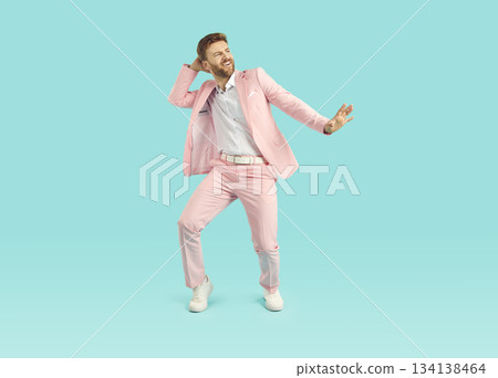 Portrait of a happy, funny young man in a pink suit dancing on a blue background Portrait of a happy, funny young man in a pink suit dancing on a blue background 134138464