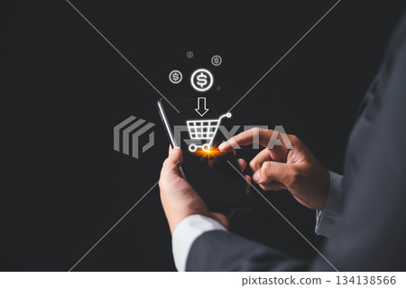 A businessman using a smartphone with a glowing virtual shopping cart icon, representing mobile ecommerce, digital payment and online purchasing technology for modern business and retail solutions. 134138566