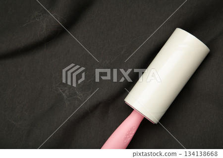 Lint roller resting on a dark suit jacket to remove pet animal hair. Lint roller resting on a dark suit jacket to remove pet animal hair. 134138668