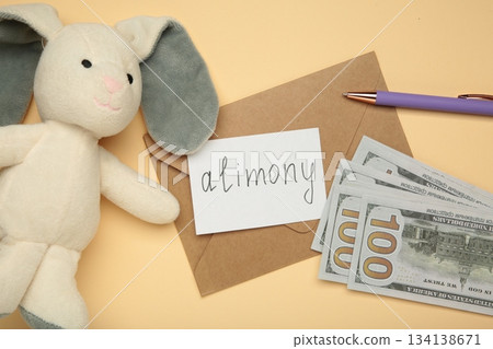 Toy bunny and envelope with word Alimony and money on beige background Toy bunny and envelope with word Alimony and money on beige background 134138671