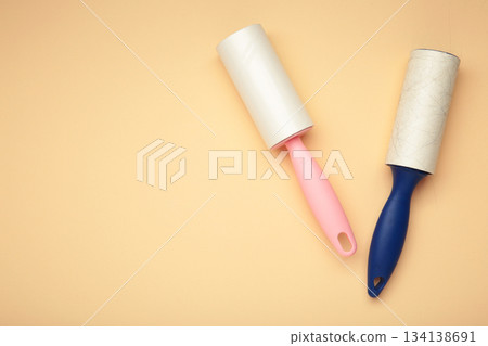 Cloth fabrics cleaner lint roller brush with paper roll on beige background. Sticky roller, pet cat dog fur dust hair remover Cloth fabrics cleaner lint roller brush with paper roll on beige background. Sticky roller, pet cat dog fur dust hair remover 134138691