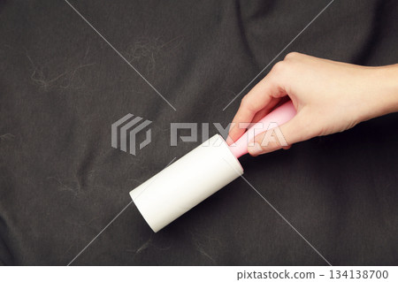 Woman cleaning black clothes background texture. Sticky roller, pet cat dog fur dust hair remover 134138700