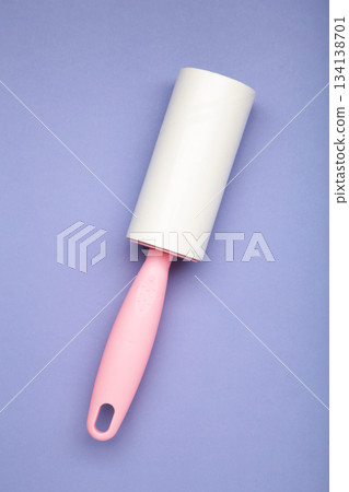 Cloth fabrics cleaner lint roller brush with paper roll on purple background. Sticky roller, pet cat dog fur dust hair remover Cloth fabrics cleaner lint roller brush with paper roll on purple background. Sticky roller, pet cat dog fur dust hair remover 134138701