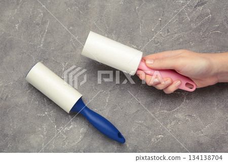 Woman holding lint roller on grey concrete background. Top view Woman holding lint roller on grey concrete background. Top view 134138704