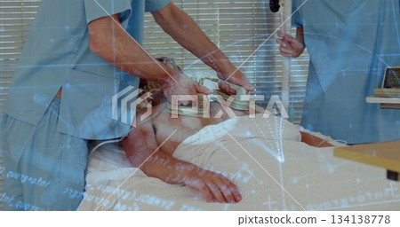 Defibrillating scrubclad team applying paddles and steadying IV pole to patient on ward bed 134138778