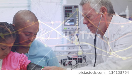 Examining senior doctor using stethoscope on girl's arm in hospital room, with vital signs monitor 134138794