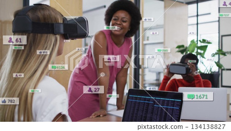 Collaborating colleagues testing VR headsets at conference table in office, with floating icons 134138827