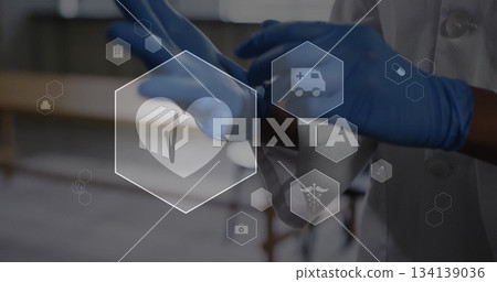 Pulling on blue nitrile gloves healthcare professional wearing labcoat in exam room, medical icons 134139036