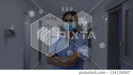 nurse crossing arms in hospital corridor, with blue scrubs mask stethoscope and hexagonal icons nurse crossing arms in hospital corridor, with blue scrubs mask stethoscope and hexagonal icons 134139087