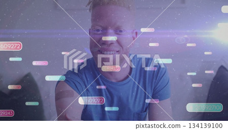 Smiling man in blue tee, gray headband sitting on sofa in living room with holographic codes 134139100