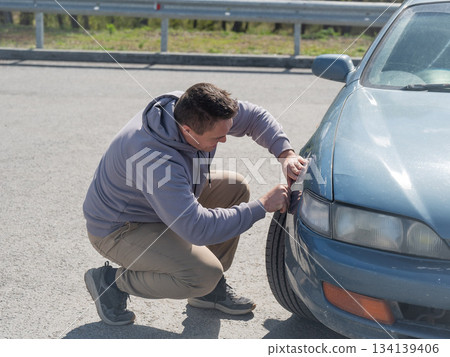 A Caucasian man tries to repair damage to a car body with his hands. A Caucasian man tries to repair damage to a car body with his hands. 134139406
