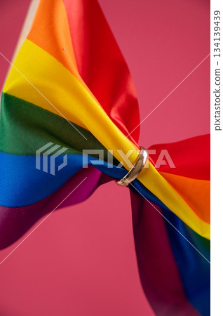 Rainbow flag held by wedding ring on pink background. Rainbow flag held by wedding ring on pink background. 134139439