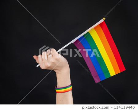 Woman with wedding ring holding rainbow flag on black background. Woman with wedding ring holding rainbow flag on black background. 134139440