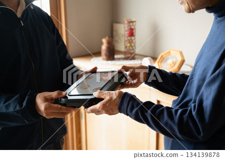 An elderly woman receiving a home-delivered lunch box An elderly woman receiving a home-delivered lunch box 134139878