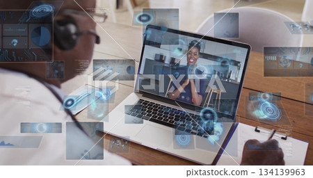 Writing doctor wearing stethoscope and headset at office desk with clipboard and laptop, copy space 134139963