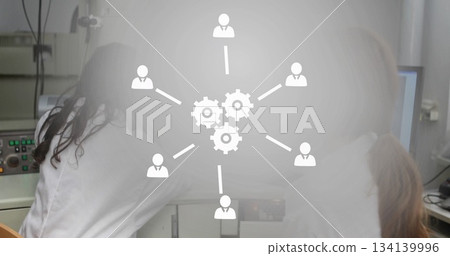 Lab technicians operating computer monitor and microscope in research lab, with network overlay 134139996