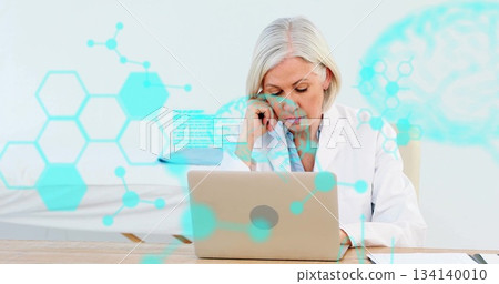 Analyzing data doctor wearing white coat viewing laptop at desk in exam room with teal overlays Analyzing data doctor wearing white coat viewing laptop at desk in exam room with teal overlays 134140010