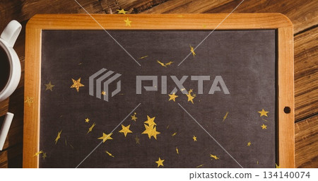 Featuring framed chalkboard lying flat on tabletop, with gold star confetti, coffee mug and chalk 134140074